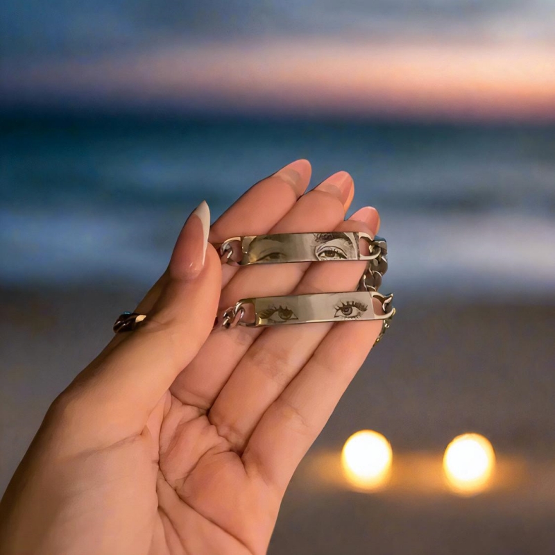 Two engraved Held Gaze bracelets held at sunset, eyes catching the last light